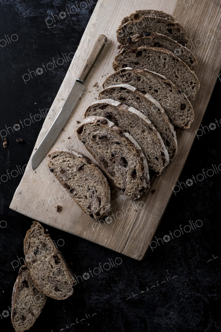 A loaf of fresh sliced brown bread on a bread board and a sharp knife