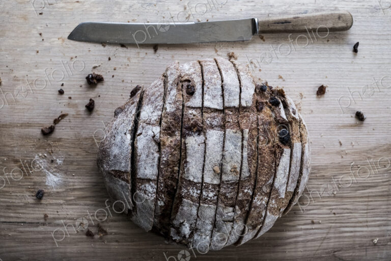 A loaf of fresh sliced brown bread on a bread board and a sharp knife