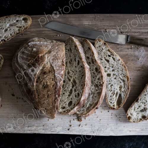 A loaf of fresh sliced brown bread on a bread board and a sharp knife A loaf of fresh sliced brown bread on a bread board and a sharp knife