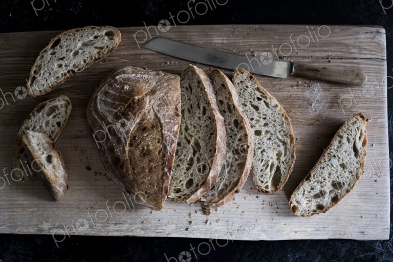 A loaf of fresh sliced brown bread on a bread board and a sharp knife