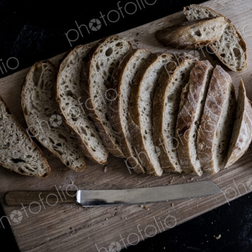 A loaf of fresh sliced brown bread on a bread board and a sharp knife A loaf of fresh sliced brown bread on a bread board and a sharp knife