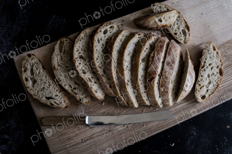 A loaf of fresh sliced brown bread on a bread board and a sharp knife