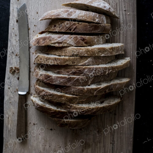 A loaf of fresh sliced brown bread on a bread board and a sharp knife A loaf of fresh sliced brown bread on a bread board and a sharp knife