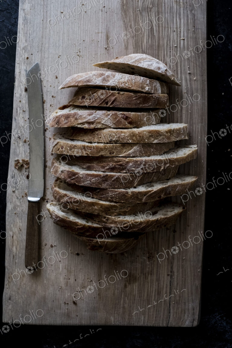 A loaf of fresh sliced brown bread on a bread board and a sharp knife