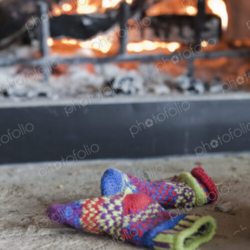 A log fire in a hearth with glowing heart, and flames. Patterned knitted woollen gloves. A log fire in a hearth with glowing heart, and flames. Patterned knitted woollen gloves.