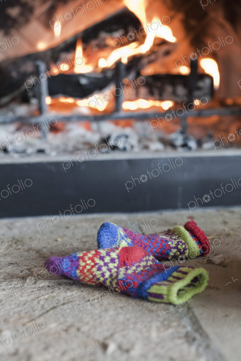 A log fire in a hearth with glowing heart, and flames. Patterned knitted woollen gloves.