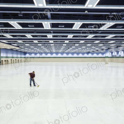 A lone man sweeping the floor of a convention center arena area.