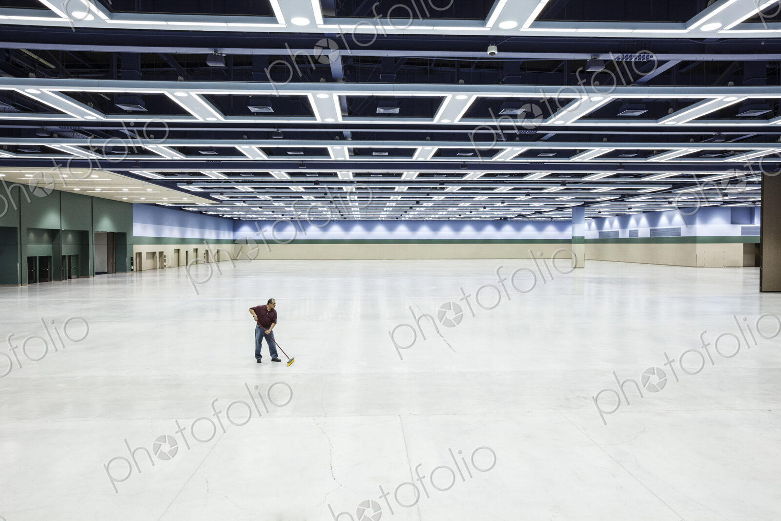 A lone man sweeping the floor of a convention center arena area.