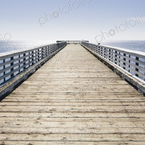 A long pier with railings extending out over the Pacific Ocean leading to the horizon. A long pier with railings extending out over the Pacific Ocean leading to the horizon.