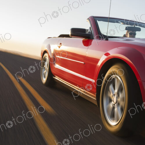 A low angle view of a convertible sports car moving on a highway late in the day. A low angle view of a convertible sports car moving on a highway late in the day.