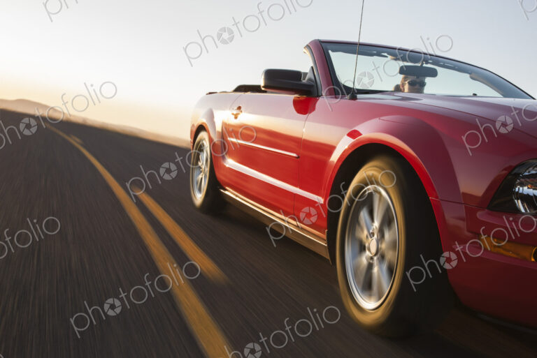 A low angle view of a convertible sports car moving on a highway late in the day.