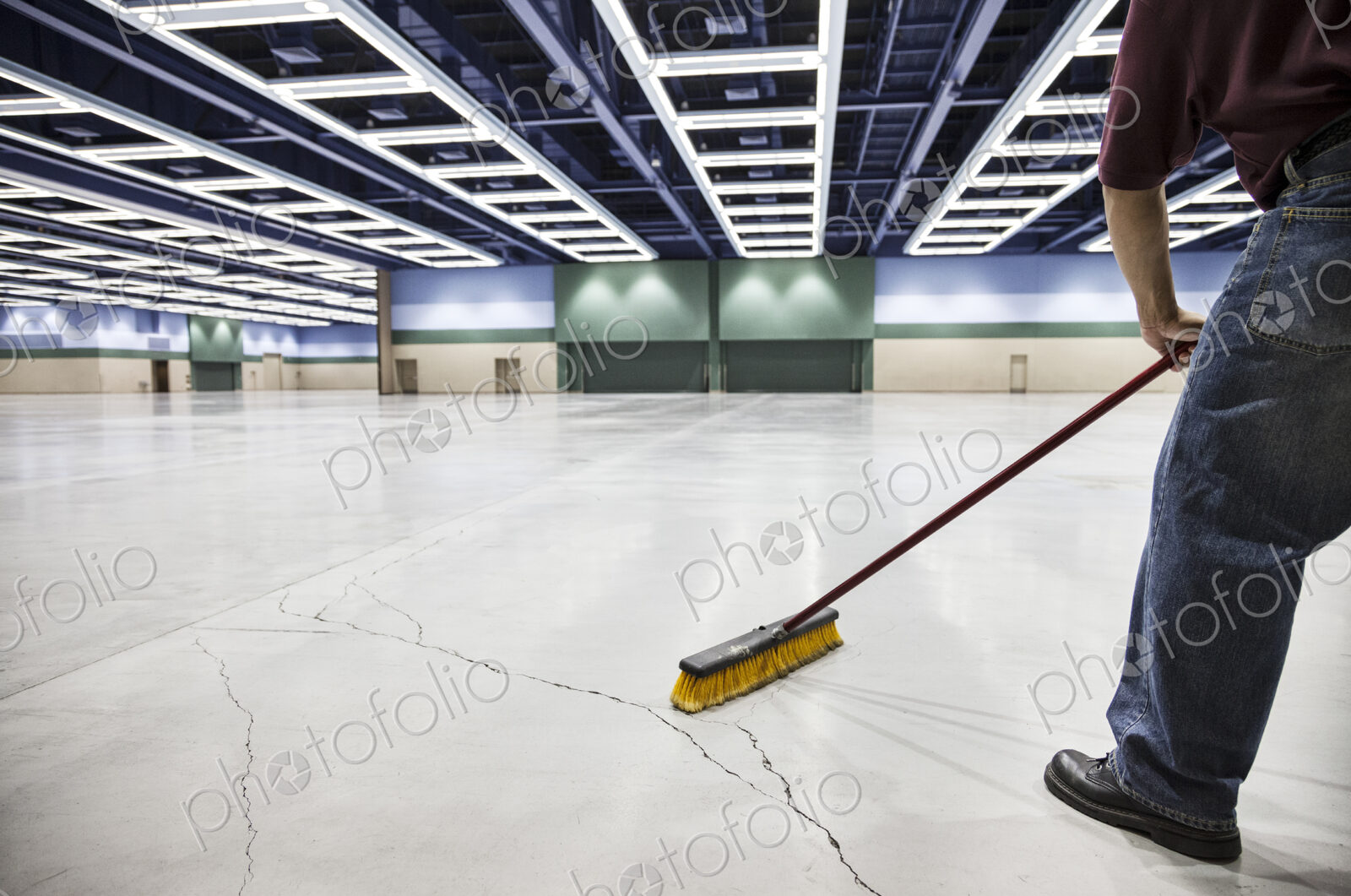 A low view closeup of a man sweeping the floor of a convention center arena.
