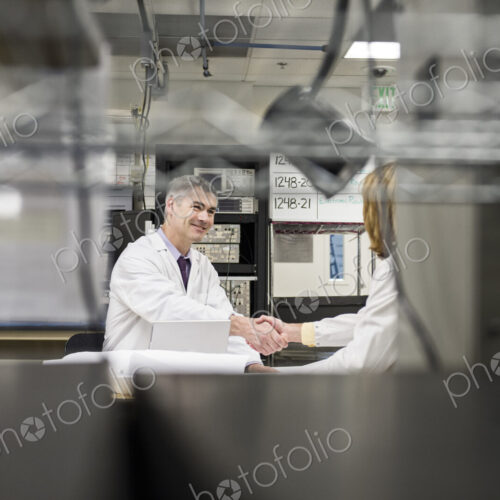 A male caucasian technician greeting a female coworker in a technical research and…