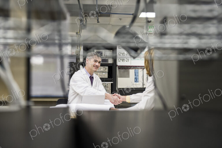 A male caucasian technician greeting a female coworker in a technical research and…