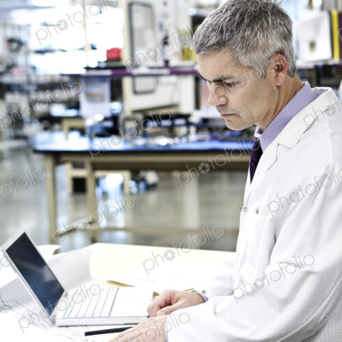A male caucasian technician in white coat using a laptop computer