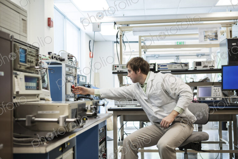 A male caucasian technician sitting at a workbench at a technical research and…