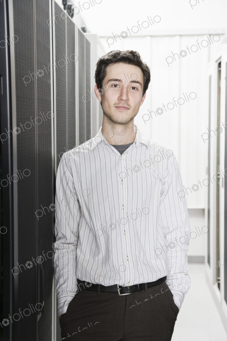 A male computer technician standing in an aisle of racks of servers in a computer…