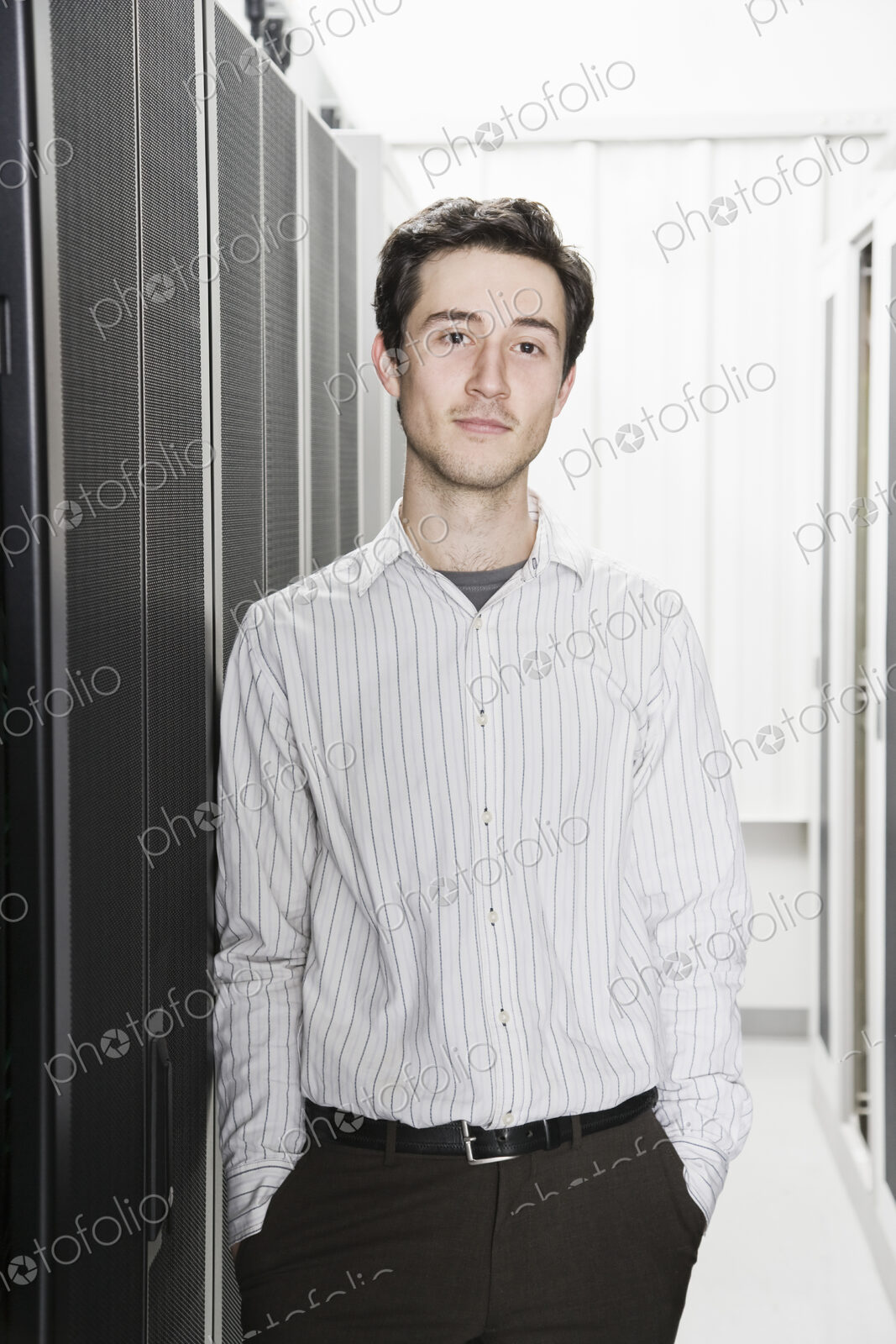 A male computer technician standing in an aisle of racks of servers in a computer…