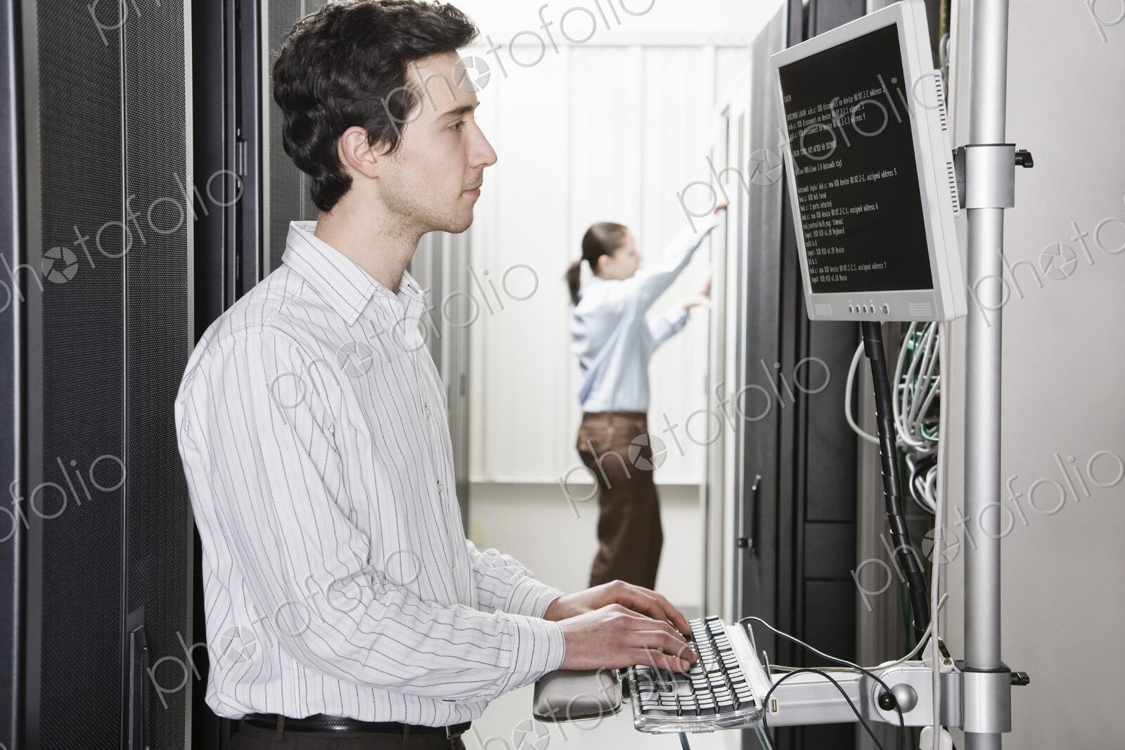 A male computer technician standing in an aisle of racks of servers in a computer…