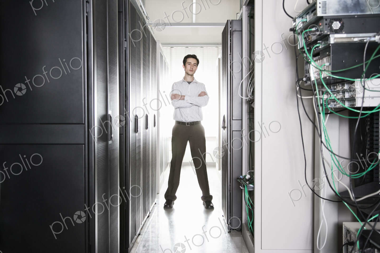 A male computer technician standing in an aisle of racks of servers in a computer…