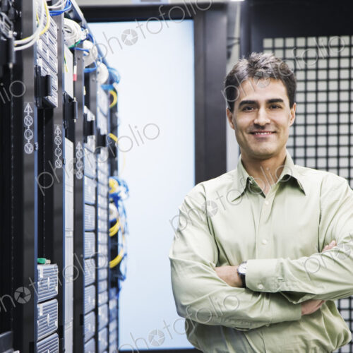 A male computer technician standing in an aisle of racks of servers in a computer… A male computer technician standing in an aisle of racks of servers in a computer…