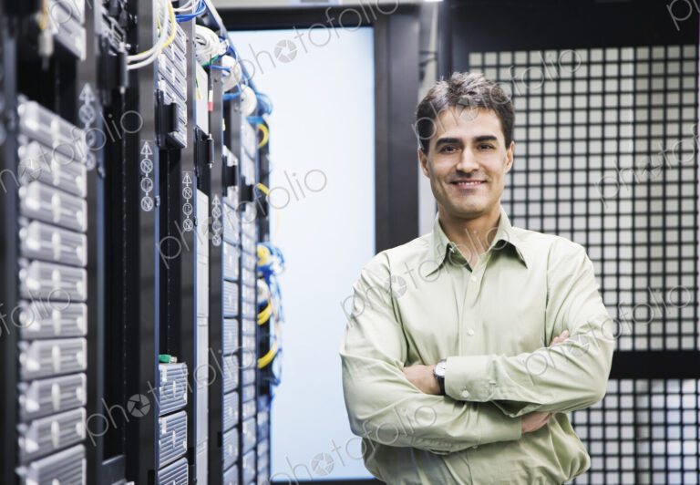 A male computer technician standing in an aisle of racks of servers in a computer…