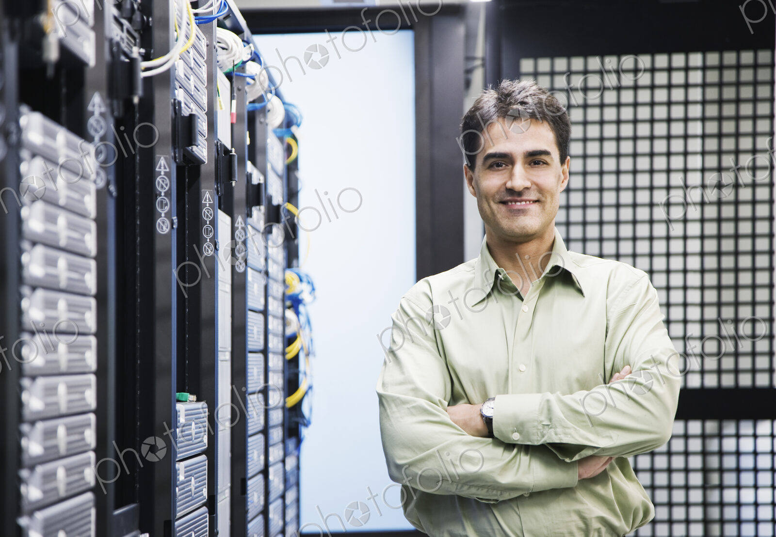 A male computer technician standing in an aisle of racks of servers in a computer…