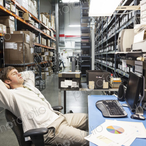 A male technician relaxing at his desk in the parts department or storage facility A male technician relaxing at his desk in the parts department or storage facility