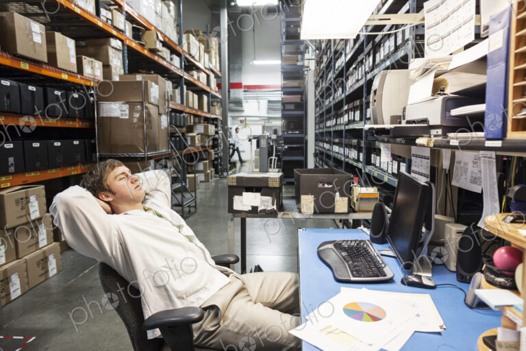 A male technician relaxing at his desk in the parts department or storage facility