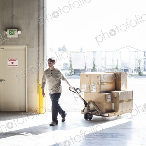 A male warehouse worker moving boxes of products using a manual pallet jack.