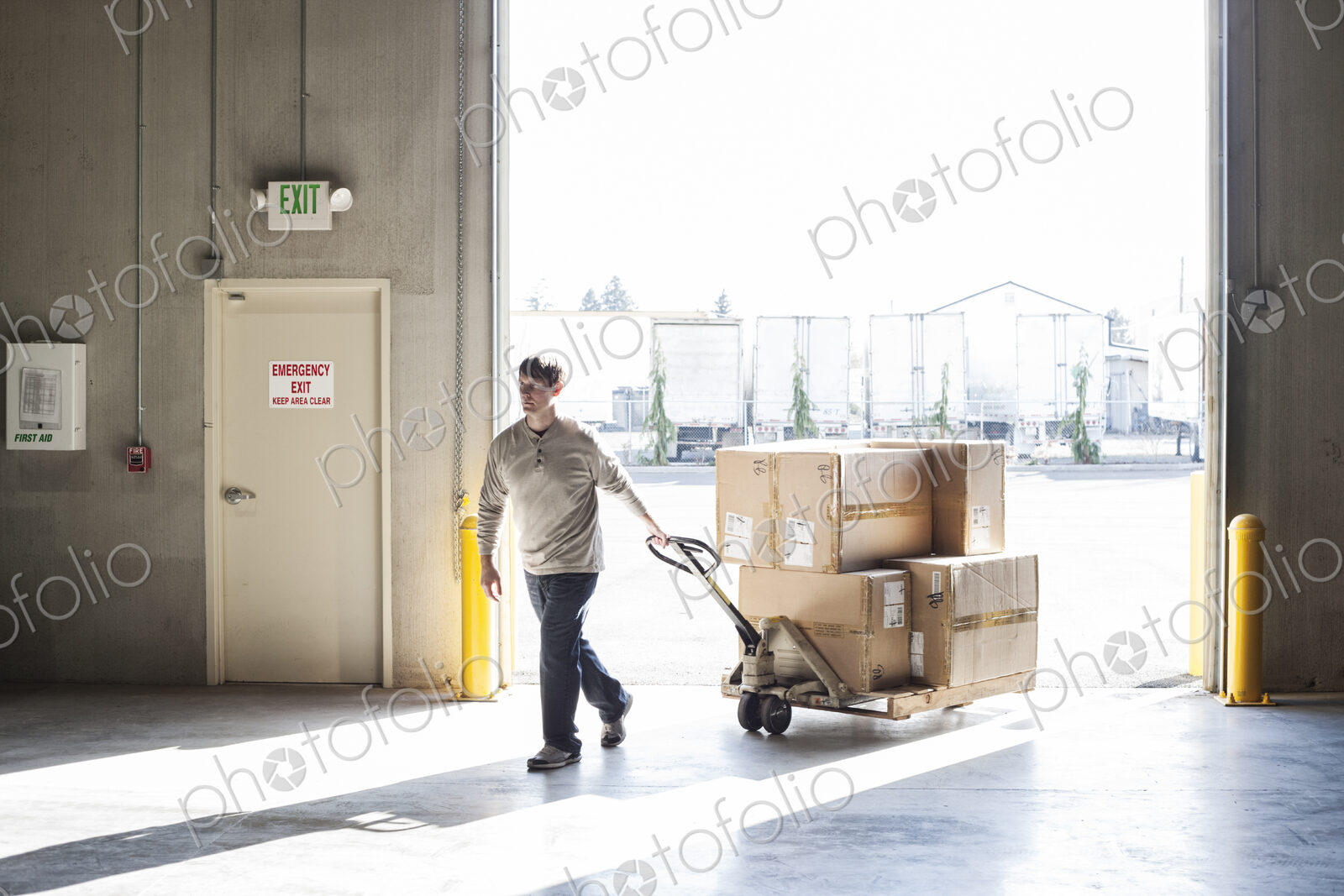 A male warehouse worker moving boxes of products using a manual pallet jack.