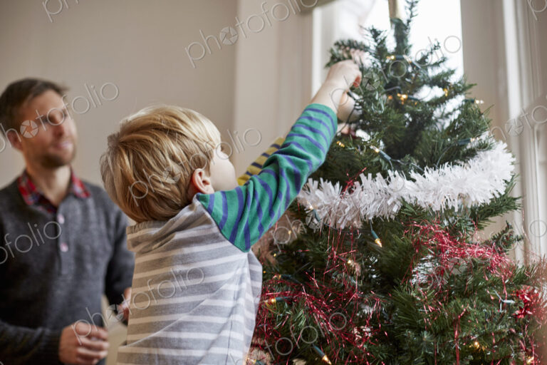 A man and a boy decorating a Christmas Tree together.