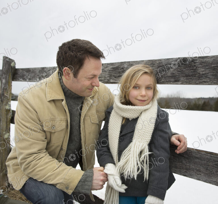 A man and a child leaning on a fence outdoors. A farm in the snow.