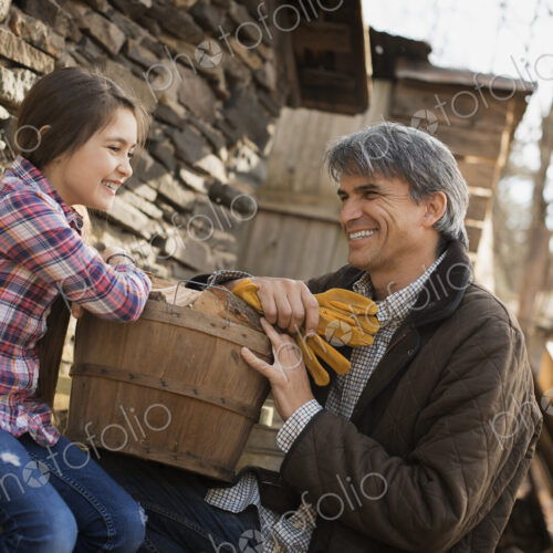 A man and a child on an organic farm. A young girl sitting on a fence, with a wooden…