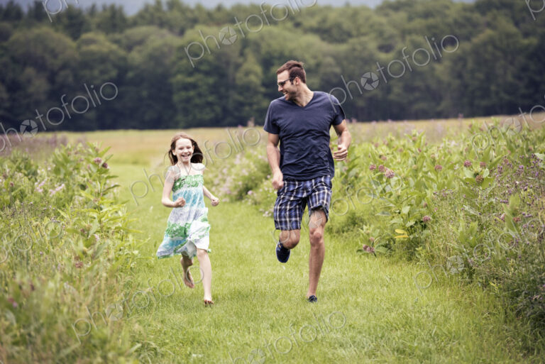 A man and a young child running through a wildflower meadow.