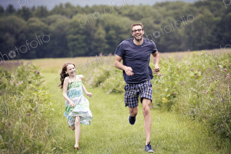 A man and a young child running through a wildflower meadow.