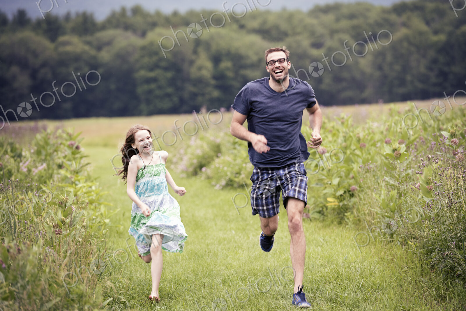 A man and a young child running through a wildflower meadow.