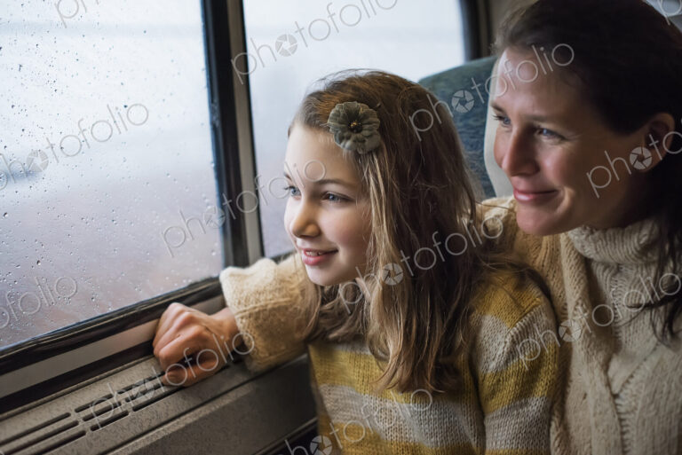 A man and a young girl sitting beside the window in a train carriage looking out at…