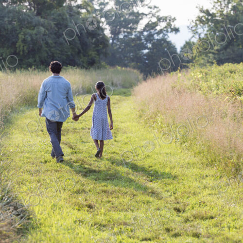 A man and a young girl walking down a mown path in the long grass holding hands. A man and a young girl walking down a mown path in the long grass holding hands.