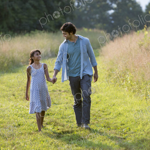 A man and a young girl walking down a mown path in the long grass holding hands. A man and a young girl walking down a mown path in the long grass holding hands.