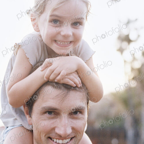 A man and his daughter smiling at the camera, the child sitting on his shoulders. A man and his daughter smiling at the camera, the child sitting on his shoulders.