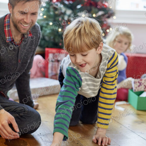 A man and two children finding and unwrapping presents on Christmas day.