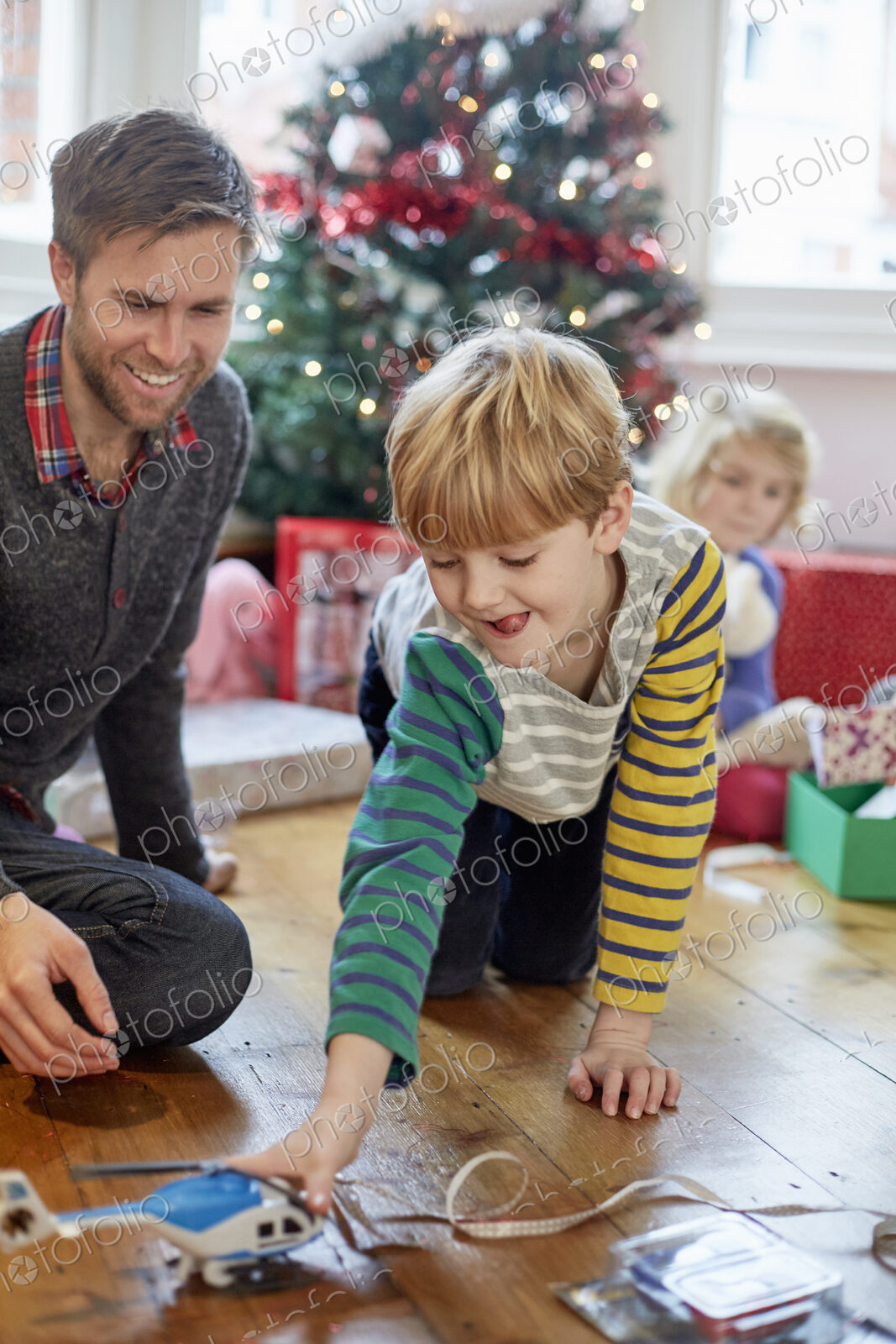 A man and two children finding and unwrapping presents on Christmas day.