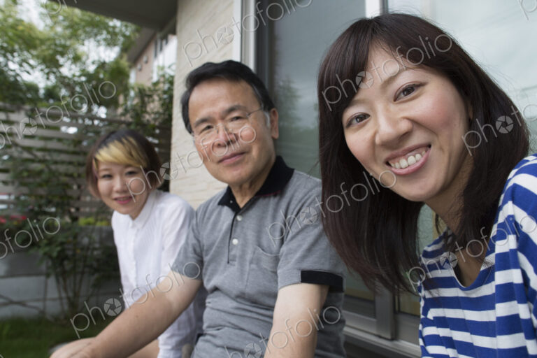 A man and two women sitting at home in a garden. A father and two daughters.