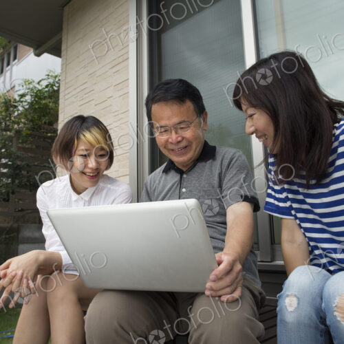 A man and two women sitting outside a house. Holding a laptop computer. A man and two women sitting outside a house. Holding a laptop computer.