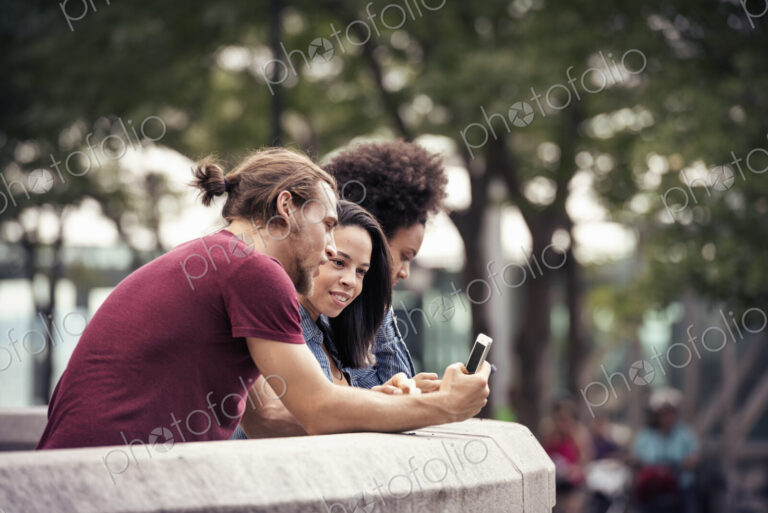 A man and two women using smart phones standing in a park