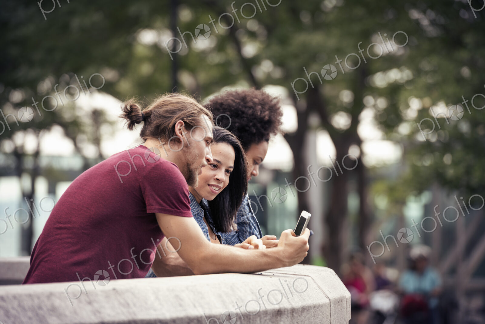 A man and two women using smart phones standing in a park