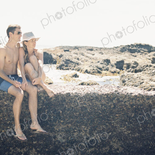 A man and woman, couple on the beach sitting on a wall by a rock pool. A man and woman, couple on the beach sitting on a wall by a rock pool.