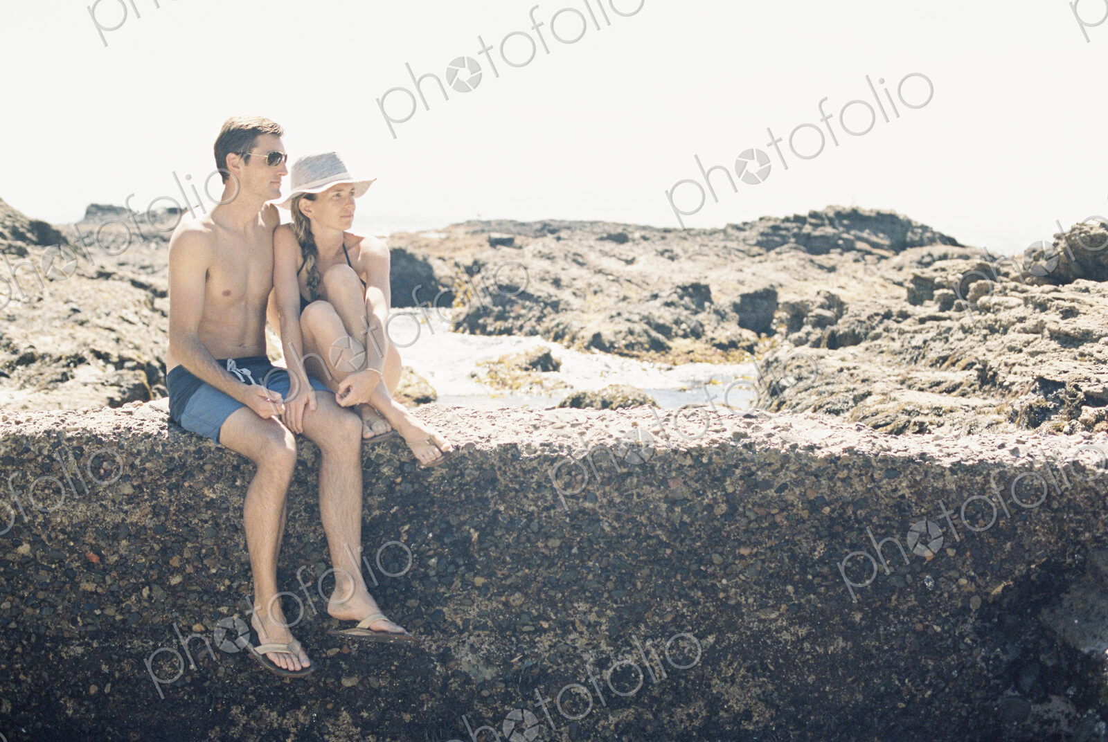A man and woman, couple on the beach sitting on a wall by a rock pool.