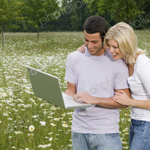 A man and woman in a flower meadow, looking at a laptop screen. A man and woman in a flower meadow, looking at a laptop screen.